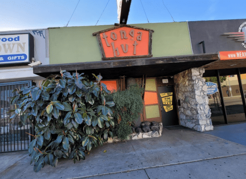 Exterior of Tonga Hut, a colorful building with a stone entrance and lush greenery in front.