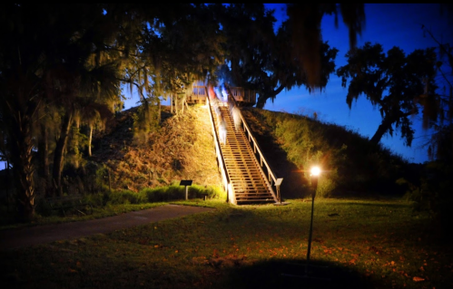 A lit staircase leads up a grassy hill at night, surrounded by trees and soft lighting.
