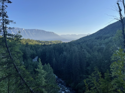 A serene landscape featuring a river winding through dense forests, with mountains in the background under a clear blue sky.