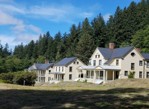 Historic houses with porches, set against a backdrop of green trees and a blue sky.