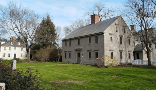 Two historic houses surrounded by trees and a grassy area under a clear blue sky.