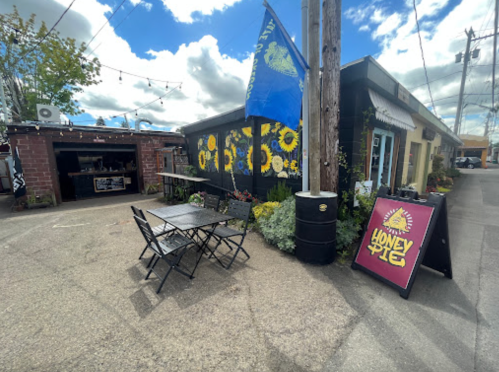 A colorful outdoor seating area with tables, a sign for "Honey Pie," and a blue flag in a vibrant alleyway.