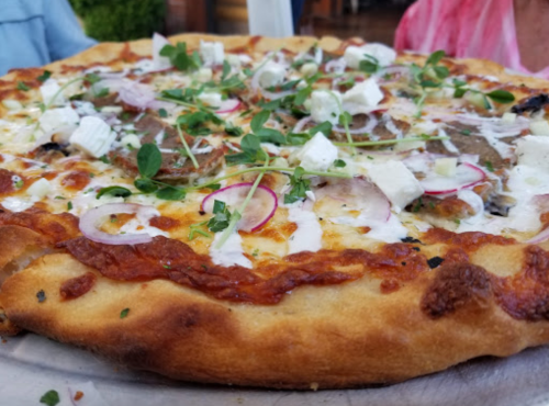 A close-up of a pizza topped with herbs, feta cheese, onions, and a creamy sauce on a golden crust.