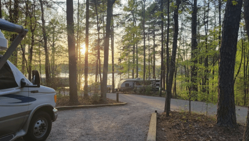 A serene campsite with RVs surrounded by trees, overlooking a lake at sunset.