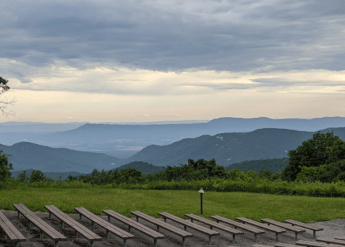 A scenic view of mountains and valleys under a cloudy sky, with empty benches in the foreground.