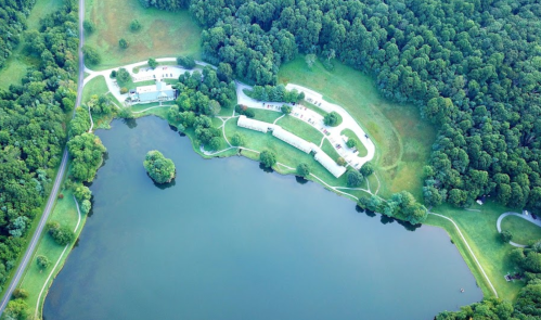 Aerial view of a serene lake surrounded by lush greenery and a small cluster of buildings along the shore.