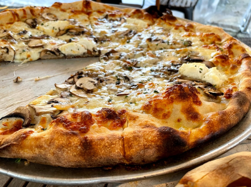 A close-up of a pizza with mushrooms and cheese, featuring a golden, crispy crust on a metal serving tray.