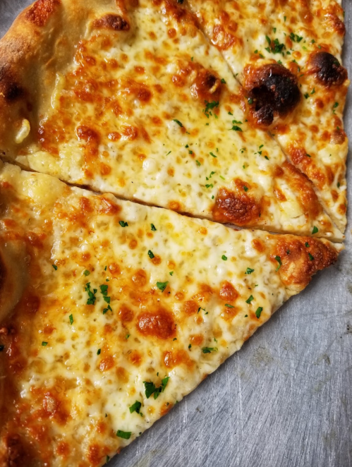 Close-up of a cheesy pizza slice with golden melted cheese and sprinkled parsley on a silver tray.