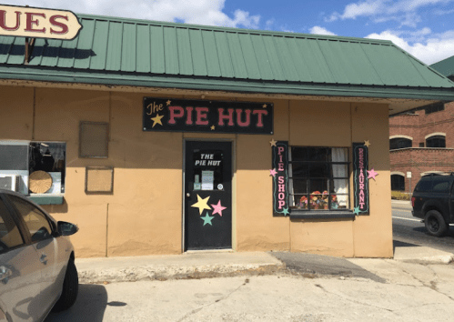 Exterior of The Pie Hut, featuring a green roof, colorful signage, and a window display with various pie-themed decorations.
