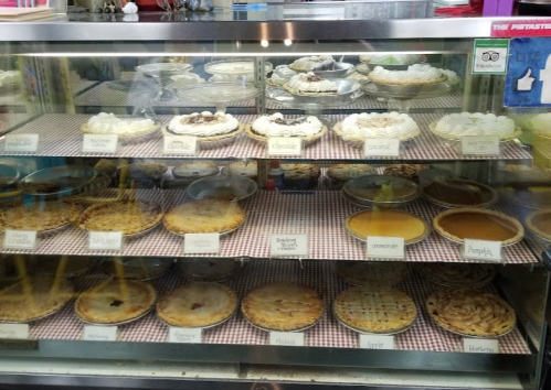 A display case filled with various pies, including chocolate, coconut, pumpkin, and apple, all labeled on a checkered cloth.