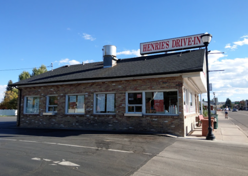 A brick building with a sign reading "Henrie's Drive-In," featuring large windows and a clear blue sky.