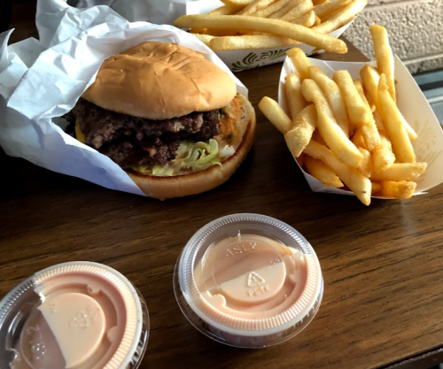 A burger with lettuce on a bun, served with a side of fries and two dipping sauces on a wooden table.