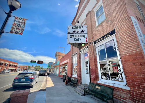A brick building with a sign for "Cowboy's Smokehouse Cafe" on a sunny street with parked cars and a blue sky.
