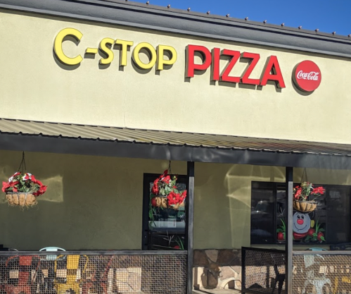 Exterior of C-Stop Pizza restaurant with colorful signage and hanging flower baskets.