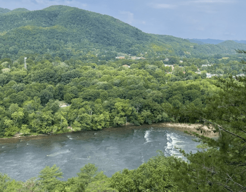 A scenic view of a river winding through lush green hills and trees under a partly cloudy sky.