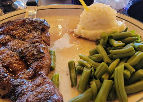 A plate with a grilled steak, mashed potatoes, and green beans, served in a casual dining setting.