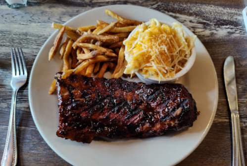 A plate with a large BBQ rib, crispy fries, and a side of cheesy mashed potatoes.