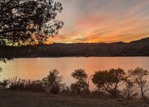 A serene lake at sunset, with colorful skies and silhouettes of trees along the shore.