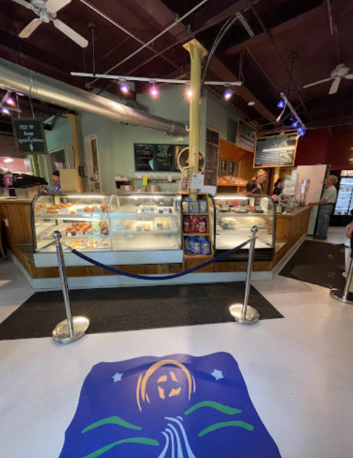 A cozy café interior with a display case of pastries, a counter, and customers in a welcoming atmosphere.