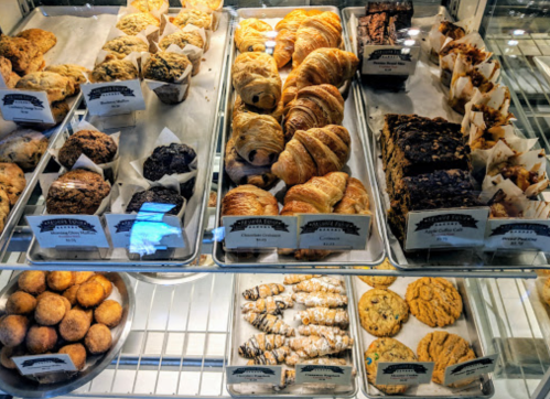 A display case filled with various baked goods, including muffins, croissants, cookies, and pastries.