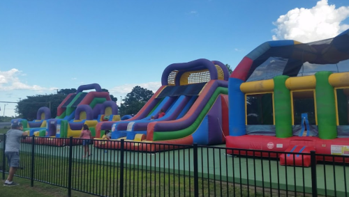Colorful inflatable bounce houses and slides set up in a park under a clear blue sky.