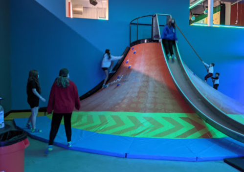 Children play on a colorful indoor slide, with some climbing and others sliding down in a vibrant, well-lit space.