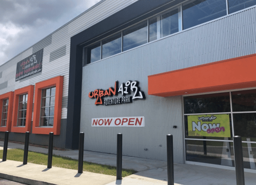 Exterior of Urban Air Adventure Park building with "NOW OPEN" signs and modern architecture.
