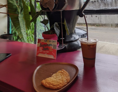 A cozy café scene featuring a cookie on a plate, an iced drink, and a colorful flyer on a pink table.