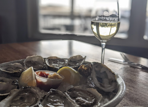 A plate of fresh oysters on ice with lemon and cocktail sauce, alongside a glass of white wine.