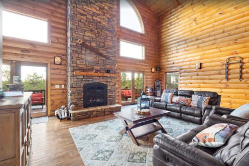 Cozy log cabin living room with a stone fireplace, large windows, and comfortable seating.
