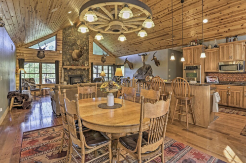 Cozy rustic dining area with wooden table, chairs, and a stone fireplace, featuring a high ceiling and natural light.