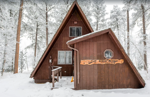 A cozy A-frame cabin named "Bobcat Retreat" surrounded by snow-covered trees.