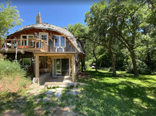 A charming round wooden house surrounded by trees and greenery on a sunny day.