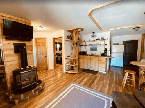 Cozy interior of a cabin featuring a wood stove, kitchen area, and wooden accents with warm lighting.