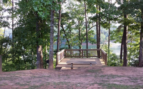 A wooden deck surrounded by trees, overlooking a calm lake in a serene natural setting.