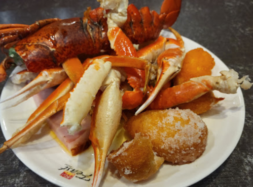 A plate of seafood featuring lobster, crab claws, and fried dough balls.