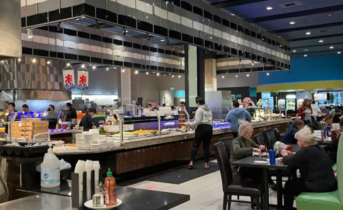 A bustling restaurant interior with a buffet, diners at tables, and staff serving food in a vibrant atmosphere.