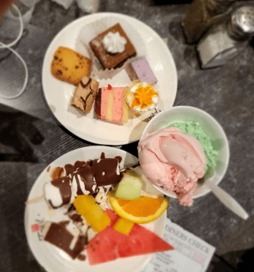 Two plates of desserts featuring cakes, ice cream, fruit, and assorted sweets on a table.
