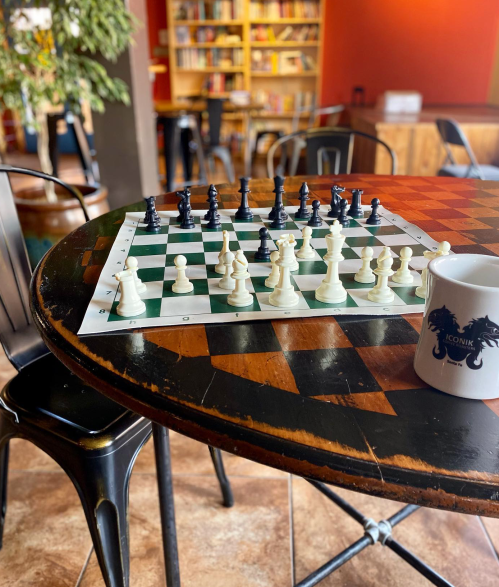 A chessboard with pieces set up on a table, a coffee mug nearby, and a cozy library background.