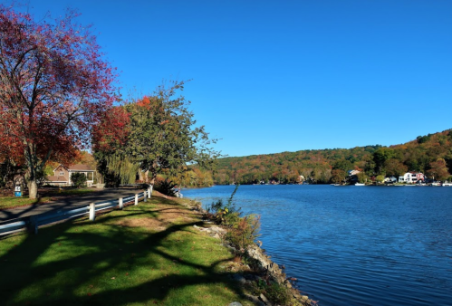 A serene lakeside view with colorful autumn trees, a clear blue sky, and a peaceful shoreline.