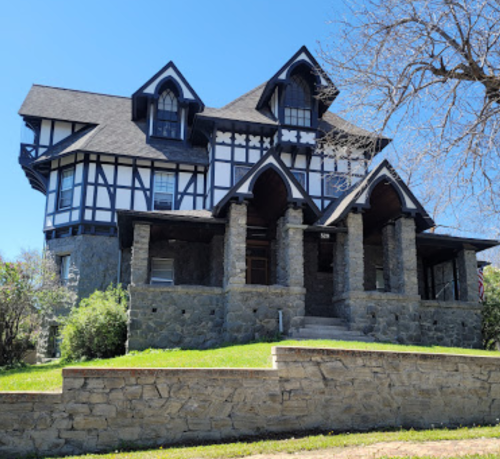 A large, historic house with a mix of stone and timber framing, featuring arched doorways and a manicured lawn.