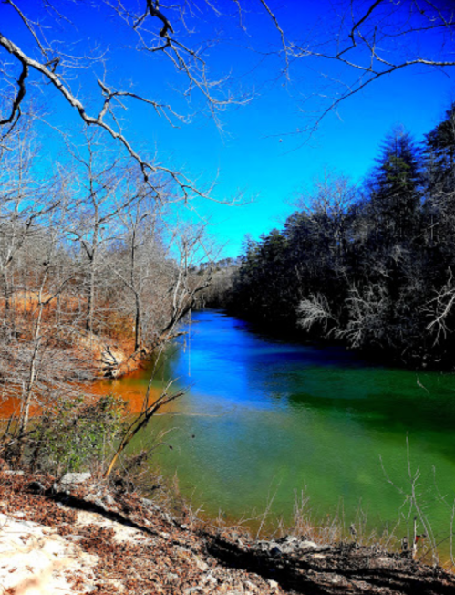 A serene river flows through a wooded area, with vibrant blue skies and bare trees lining the banks.