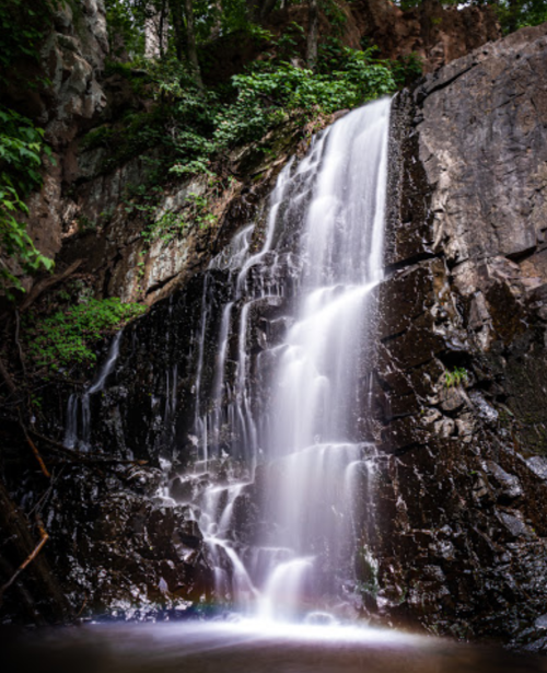 A serene waterfall cascading over rocky cliffs, surrounded by lush greenery and a tranquil pool at the base.