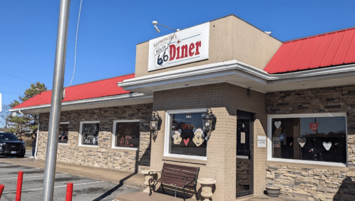 Exterior of a diner with a red roof, stone walls, and a sign reading "Route 66 Diner," featuring heart decorations in windows.