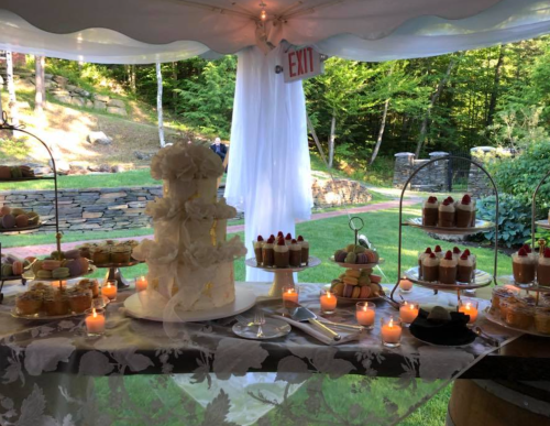 A beautifully arranged dessert table featuring a white cake, cupcakes, and candles, set outdoors under a tent.