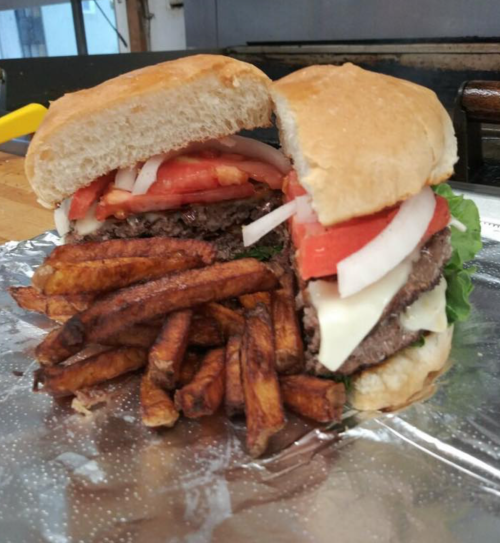 A juicy hamburger with lettuce, tomato, and onion, served with crispy fries on the side, wrapped in foil.