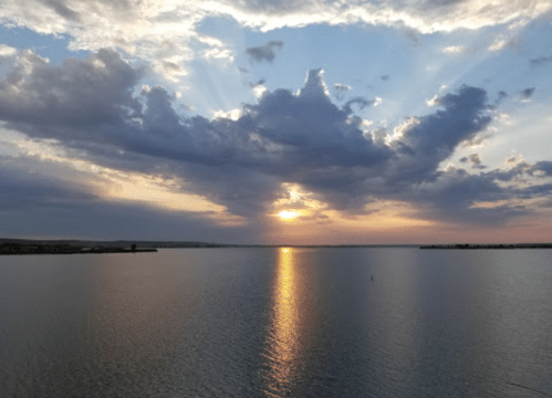 Sunset over a calm lake, with rays of light breaking through clouds and reflecting on the water's surface.