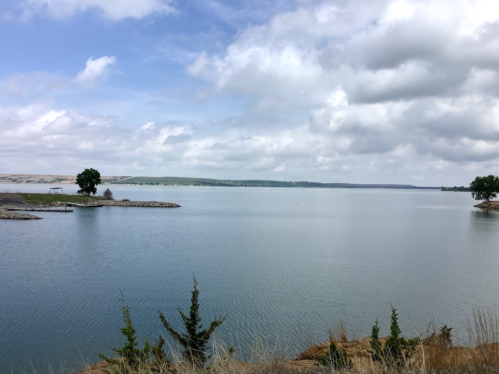 A serene lake surrounded by greenery and distant hills under a partly cloudy sky.
