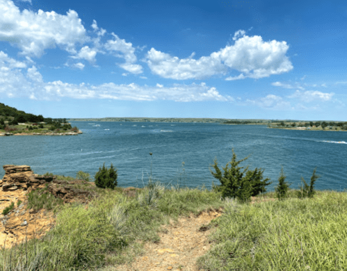 A scenic view of a lake surrounded by greenery and hills under a partly cloudy sky.