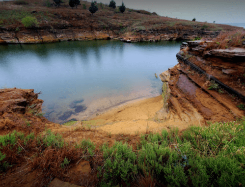 A serene landscape featuring a calm body of water surrounded by rocky cliffs and lush greenery.